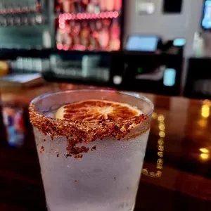 A frosty cocktail with a spicy rim and an orange slice at a bar.