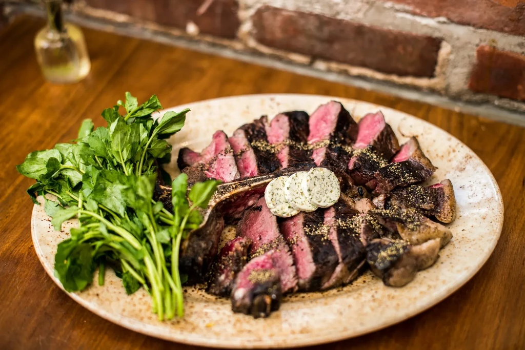 A large platter of sliced porterhouse steak with watercress and herb butter.