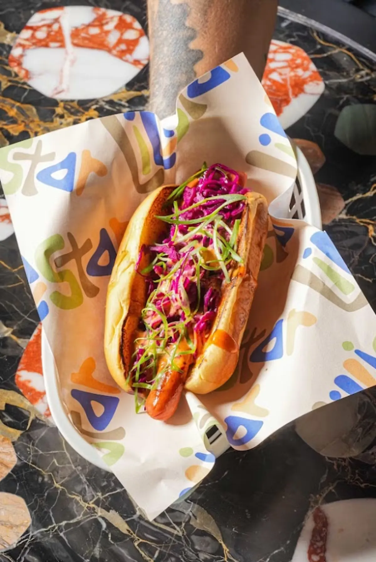 Hot dog with red cabbage and green onions on black marble table.