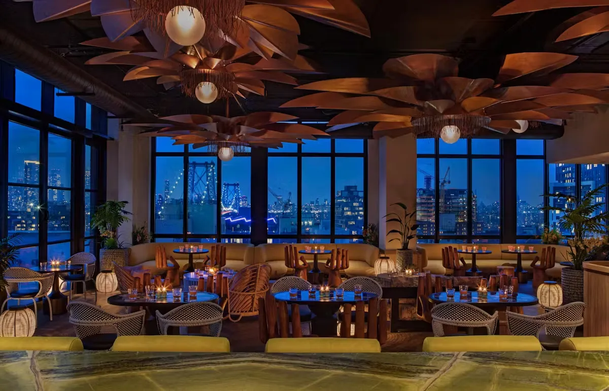 A rooftop bar with city views at dusk, large palm-leaf ceiling fixtures.