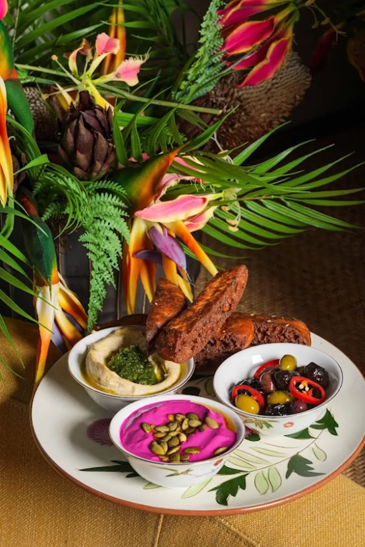 Tropical flower arrangement with pita bread and three dips on a plate.