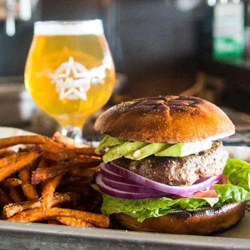 Gourmet burger, sweet potato fries, and beer on a metal tray.