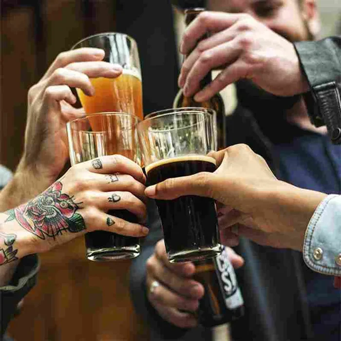Three hands, one tattooed, clink glasses and a bottle.