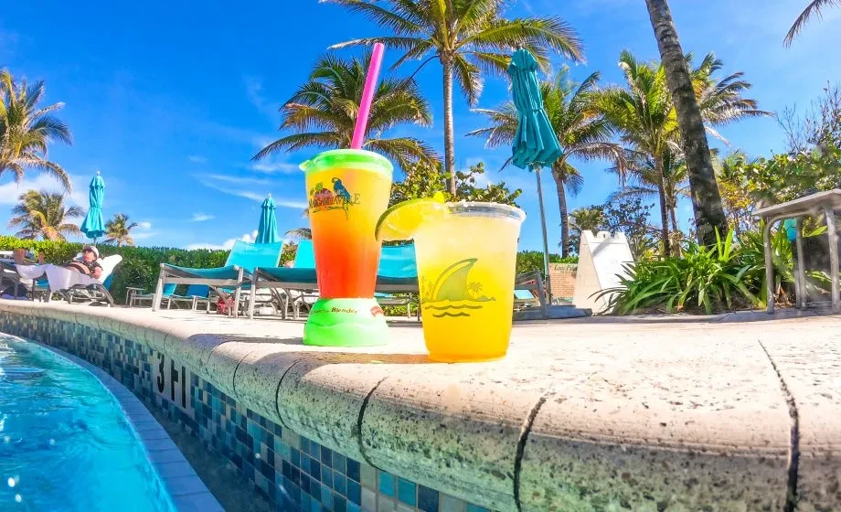 Two colorful tropical drinks sit on a pool edge at a sunny resort.