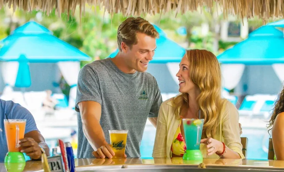 Smiling man and woman at a thatched-roof bar with drinks.