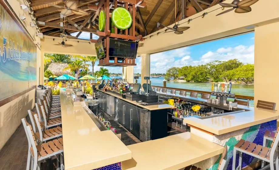 Unoccupied tropical outdoor bar by water with lime slices and mural.