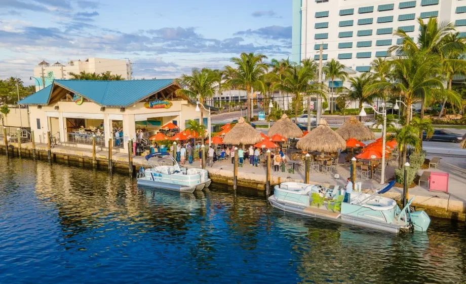 Aerial view: busy waterfront restaurant, orange umbrellas, and docked boats.