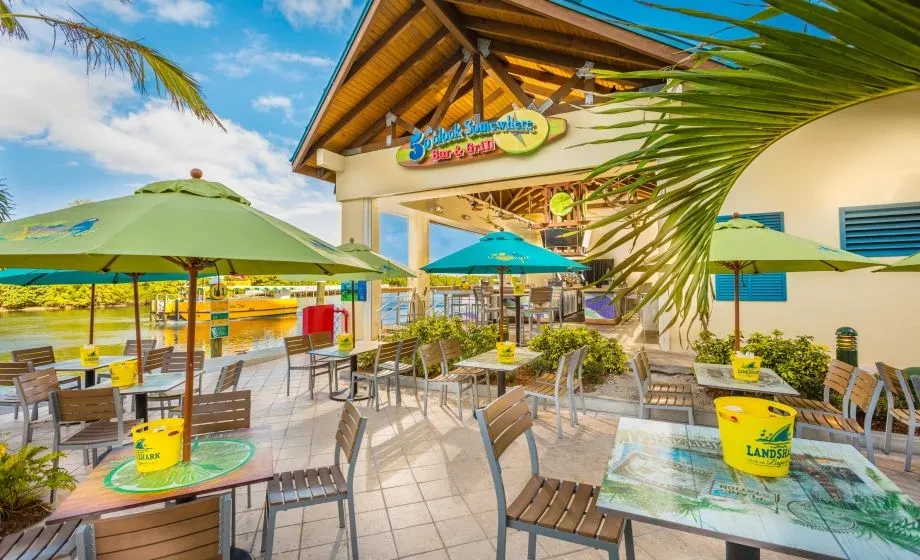 Empty, sunlit waterside patio of '5 O'Clock Somewhere Bar & Grill'.