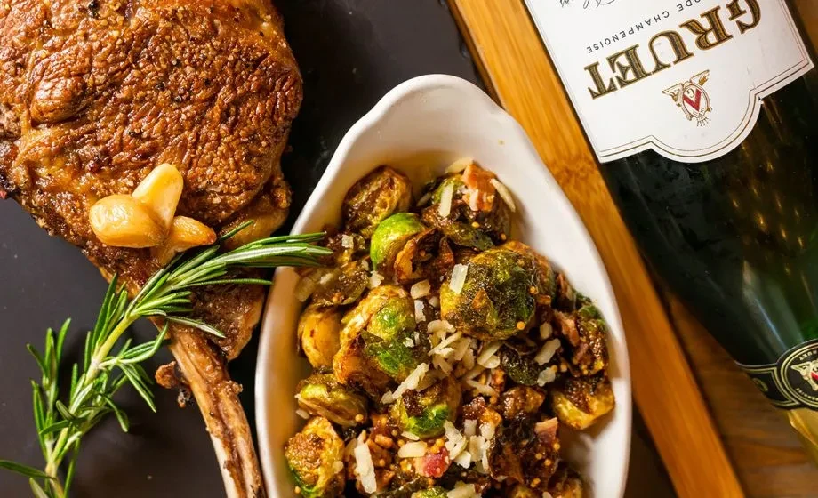 Top-down view of seared meat, roasted Brussels sprouts, and Gruet sparkling wine.