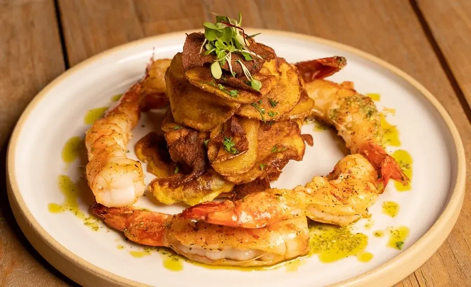 Grilled shrimp and crispy chips garnished with microgreens and sauce.