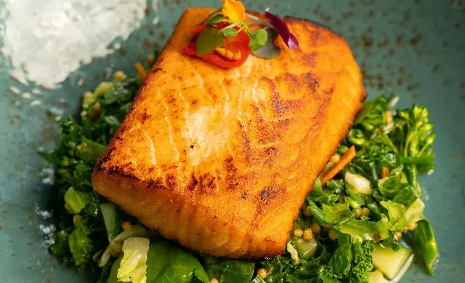 Pan-seared salmon with edible flowers, green vegetables, and grains.