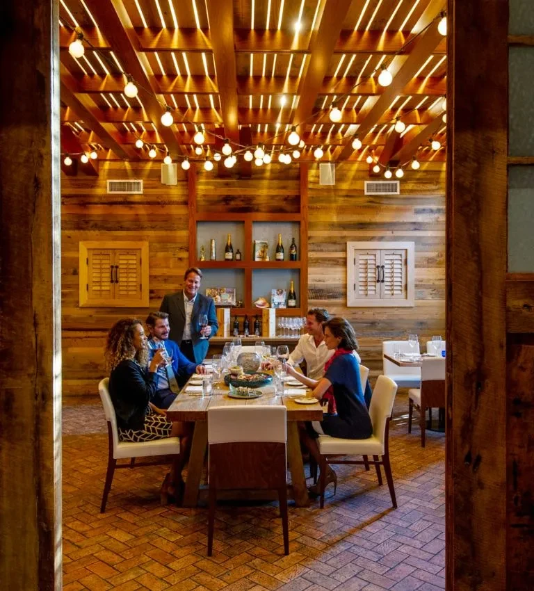 Six people dining at a rustic table in a wooden-paneled restaurant.