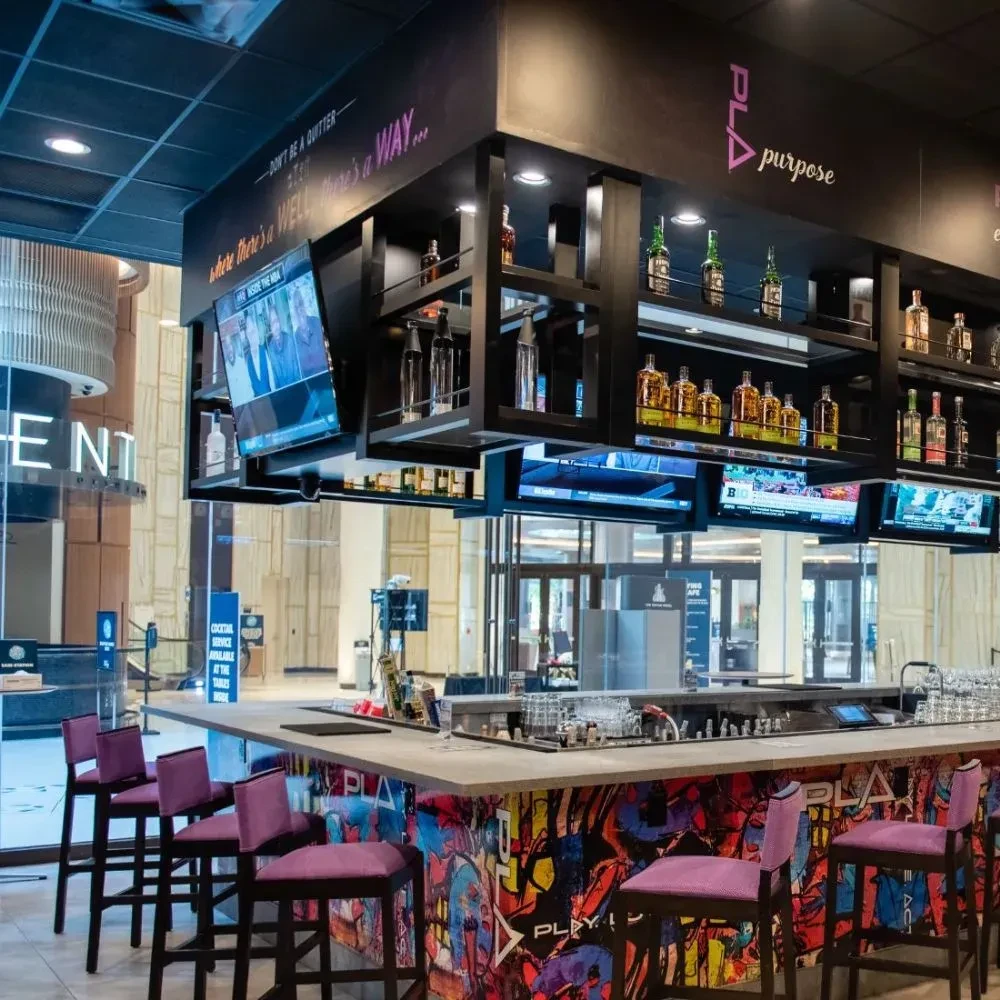 Modern bar with graffiti art, purple stools, liquor, and TVs.