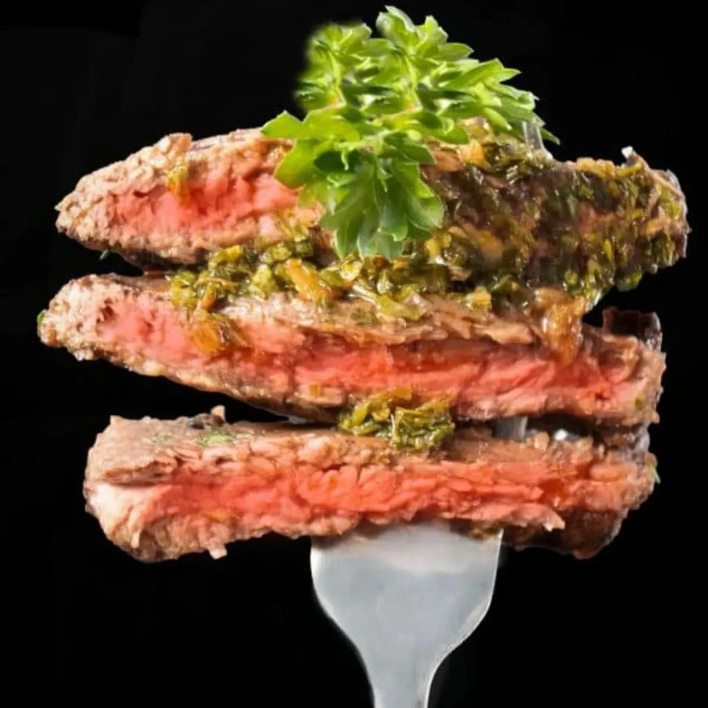 Three stacked medium-rare steak slices with chimichurri on a fork.