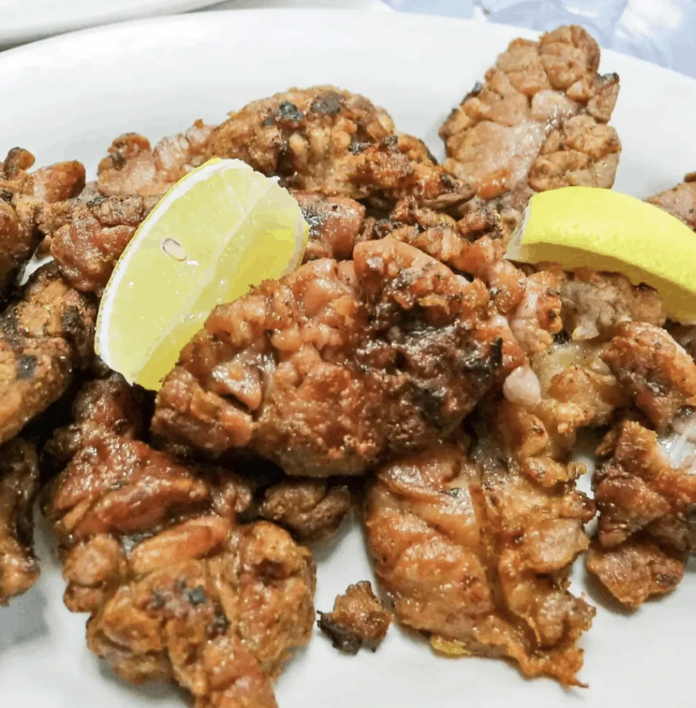 Plate of cooked meat or offal with two lemon wedges.