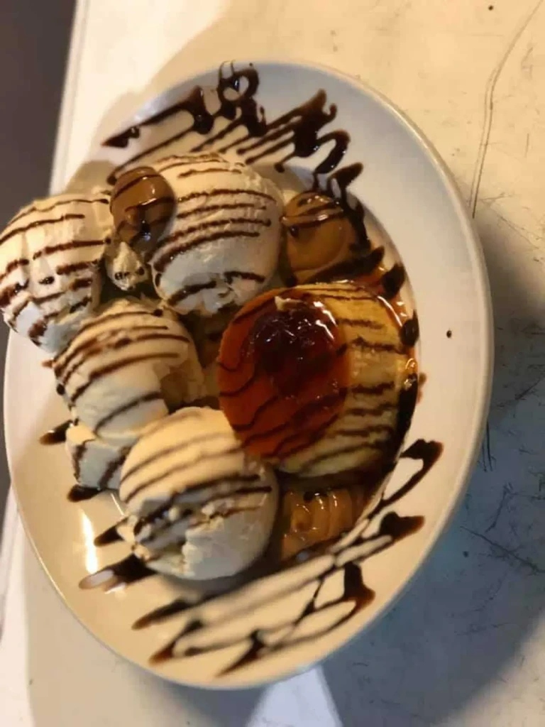 Plate of vanilla ice cream, mini pancakes, preserve, and chocolate sauce.