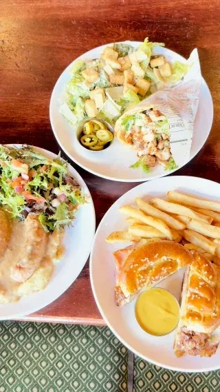 Overhead shot of three plates with salad, sandwich, and creamy main.