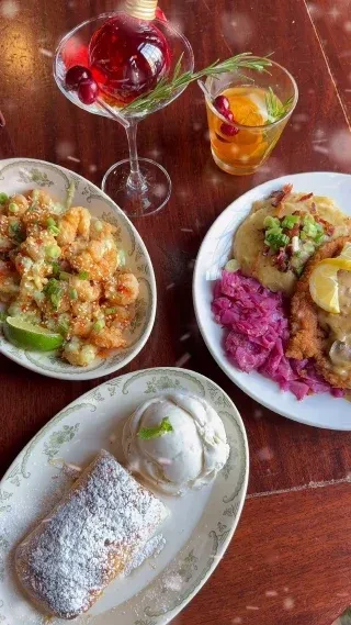 Top-down view of varied restaurant meal with cocktails, schnitzel, and dessert.