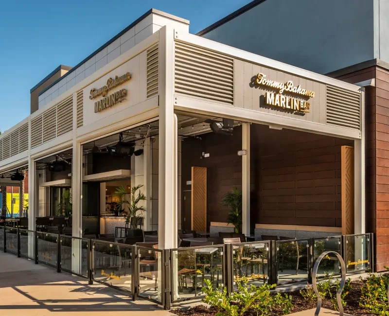 Tommy Bahama Marlin Bar exterior: modern architecture, patio seating, clear sky.