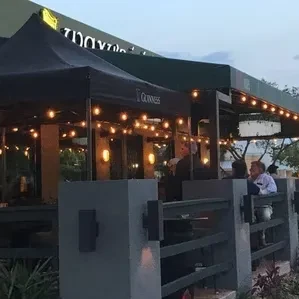Outdoor restaurant patio with Guinness tent, string lights, and indistinct people.