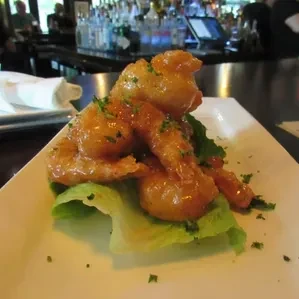 Plate of tempura shrimp with orange sauce and herbs, bar background.