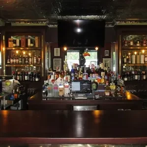 Dimly lit, well-stocked bar interior, dark wooden counter, many liquor bottles.