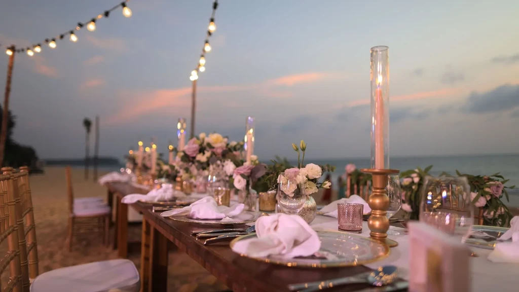 Elegant dining table set on a sandy beach at sunset.