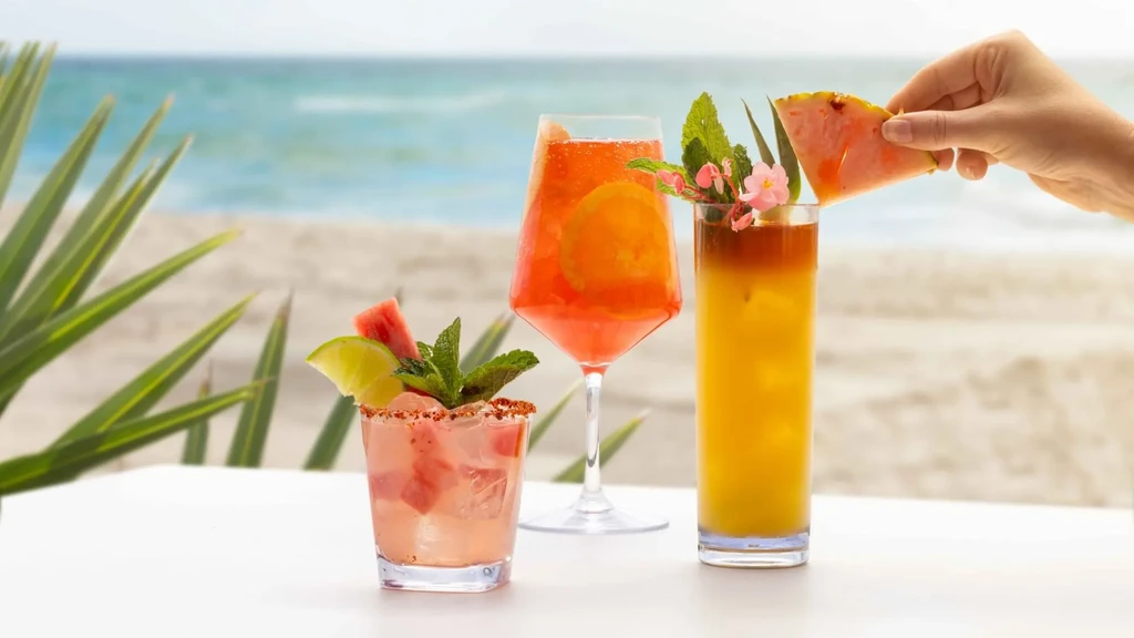 Three vibrant, garnished cocktails on a table with beach background.