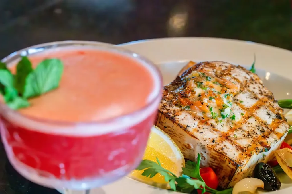 High-angle view of a plated grilled fish meal and layered drink.
