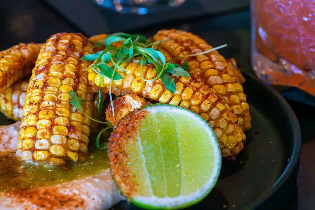 Close-up of seasoned grilled corn with lime and two sauces.