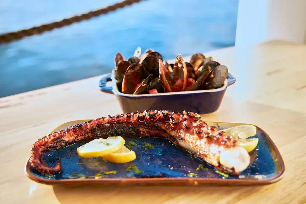 Grilled octopus and steamed mussels served on a table by the water.
