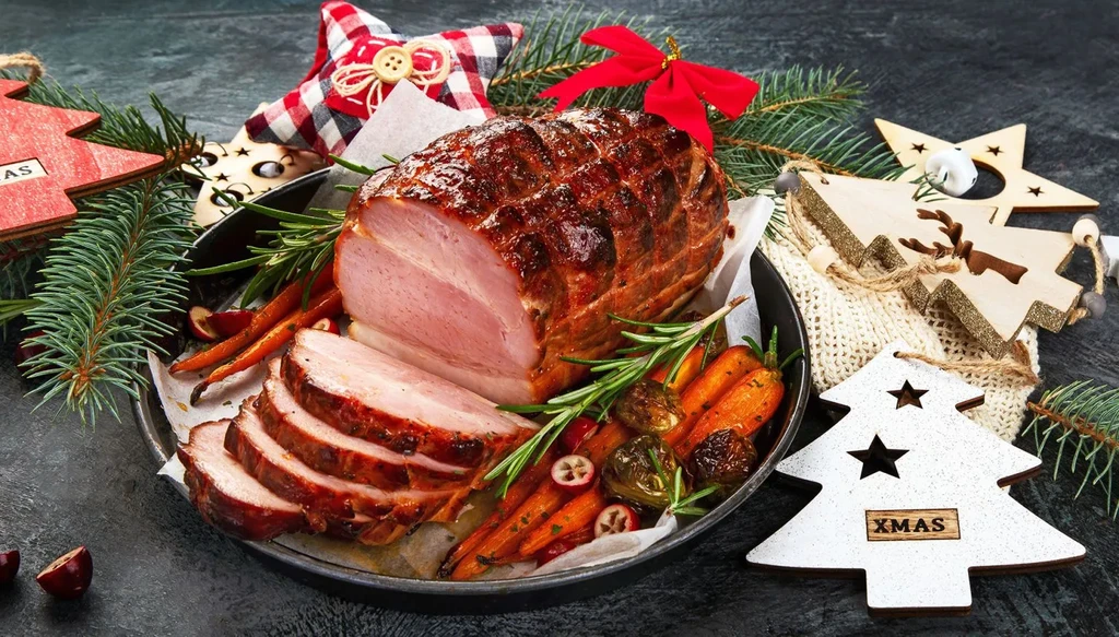 Roasted ham with carrots, cranberries, and festive Christmas decorations.