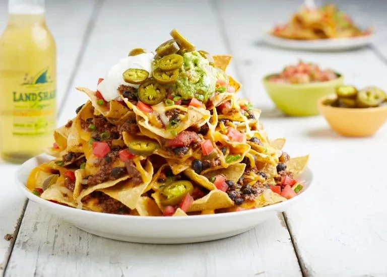 Large nachos with cheese, guacamole, and Landshark beer on a table.