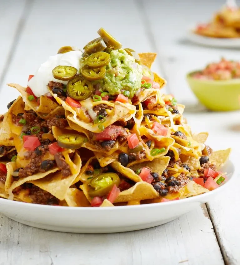 Nachos with melted cheese, meat, beans, tomatoes, jalapeños, and dips.