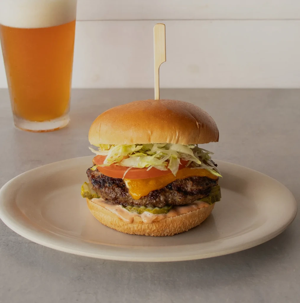 Close-up hamburger with melted cheese, lettuce, tomato, and a wooden skewer.