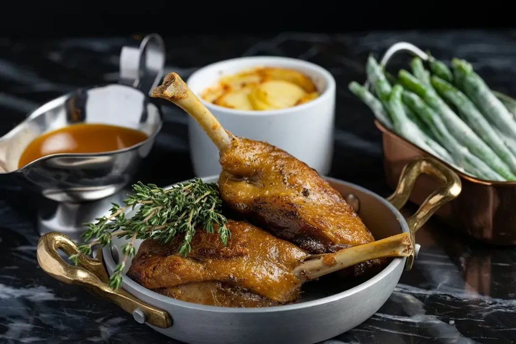 Two golden-brown poultry legs with thyme, gravy, potatoes, green beans.