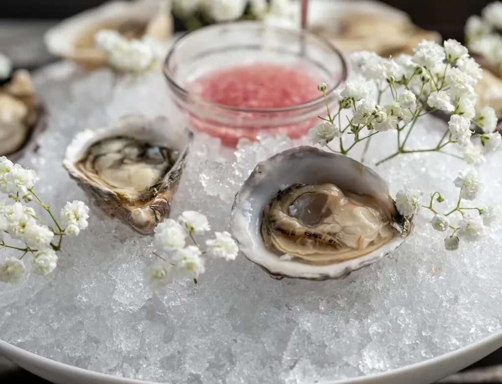 Fresh oysters on crushed ice with pink sauce and flowers.