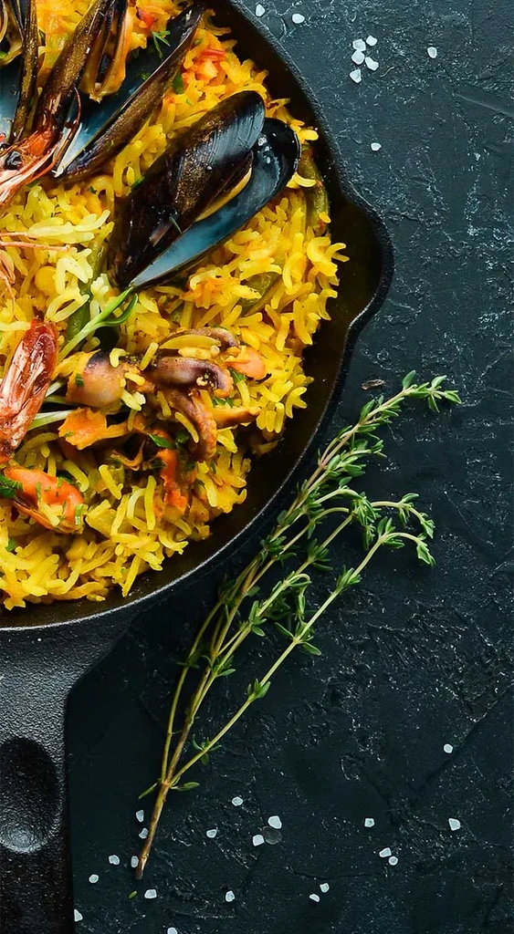 Overhead: Yellow seafood rice with mussels, shrimp, herbs in skillet.