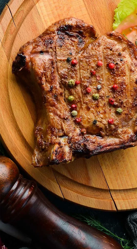Grilled steak with colorful peppercorns on a rustic wooden board.