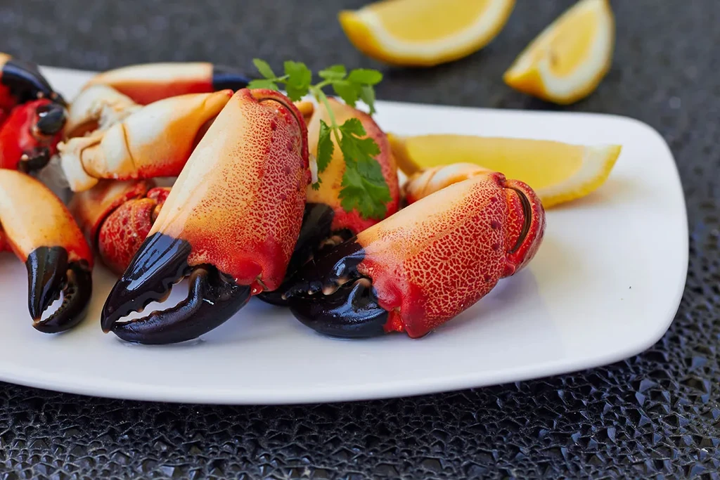 Cooked reddish-orange crab claws with lemon and parsley on a plate.