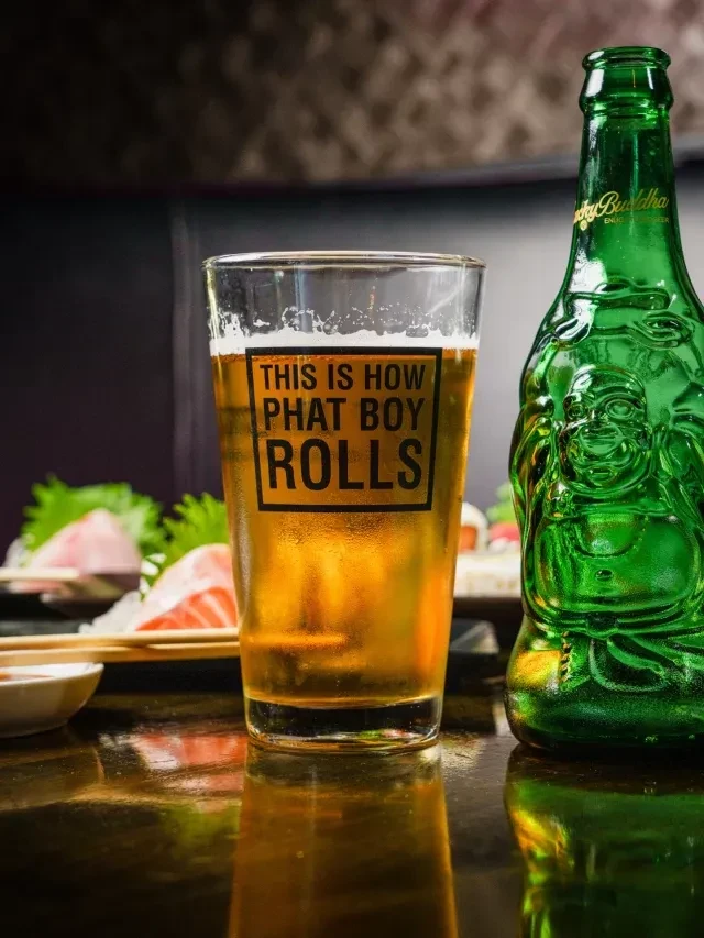 Glass of amber beer next to a Buddha-shaped Lucky Buddha bottle.