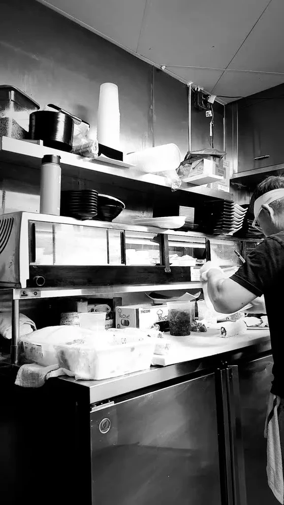 Black and white photo of a chef preparing food in a commercial kitchen.