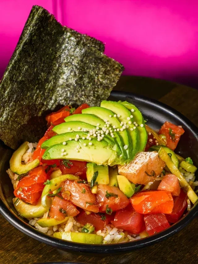 Vibrant poke bowl with fish, avocado, rice on a magenta background.