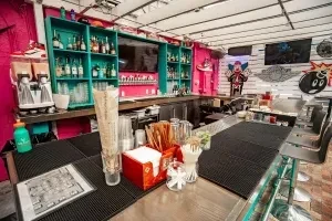 Vibrant, eclectic bar with teal shelves, hot pink walls, and street art.