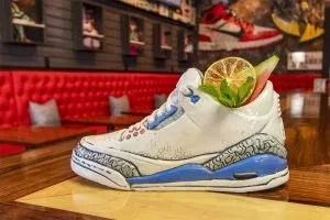 Garnished cocktail in Air Jordan 3 sneaker vessel at themed bar.