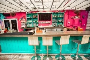 Hot pink and turquoise modern bar with bottles and stools.