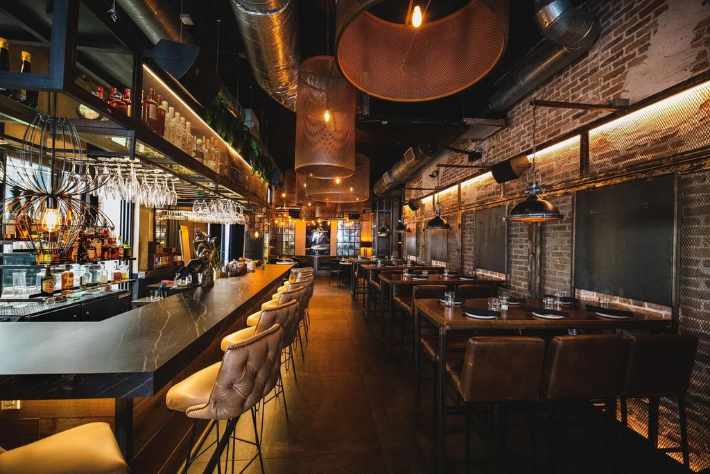Empty industrial-chic restaurant bar interior with exposed brick and warm lighting.