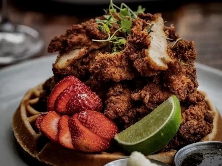 Crispy fried chicken and waffles with strawberries, lime, syrup, and sauce.