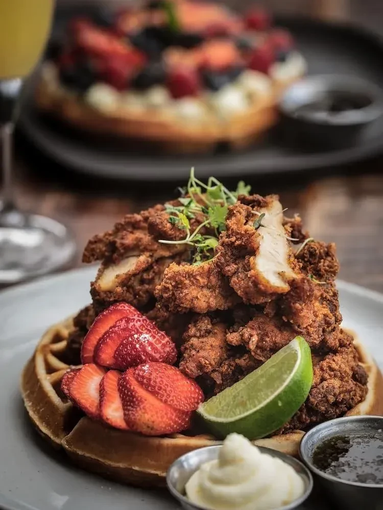 Fried chicken and waffles with strawberries, lime, cream, and syrup.