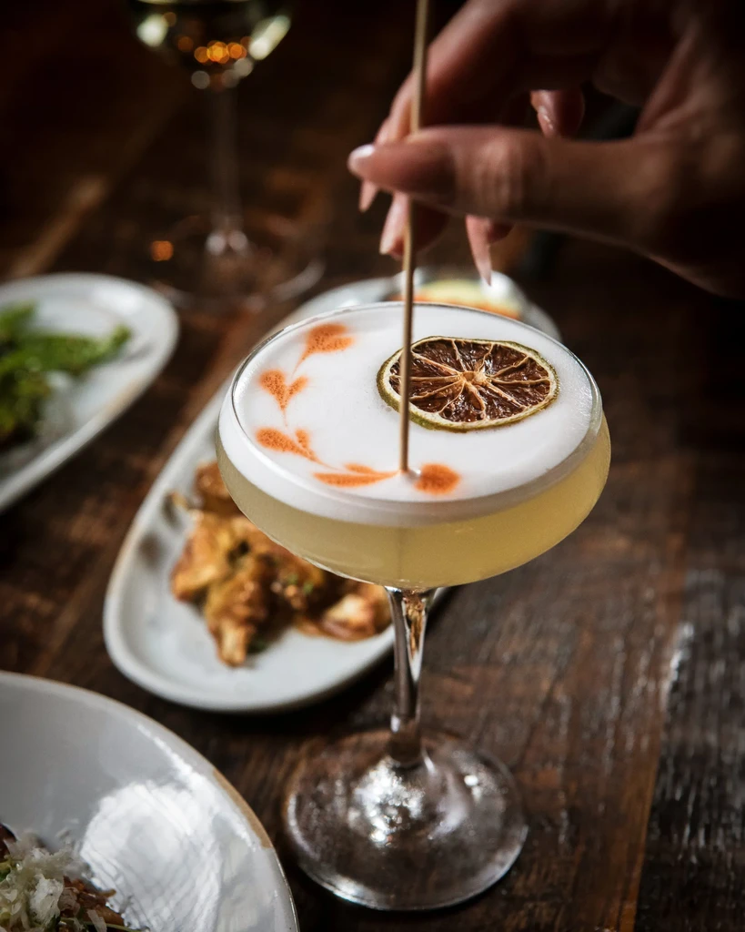 Cocktail with heart-patterned foam, dried citrus, and skewer in coupe.